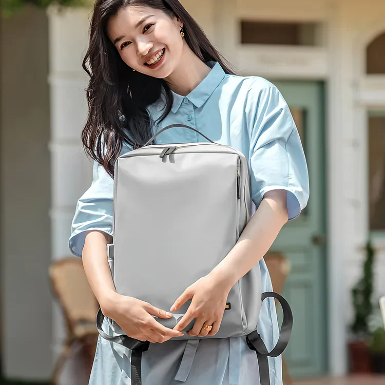 薄いグレーのビジネスリュックを抱える笑顔の女性。軽量でコンパクトなデザインが特徴のレディースリュック。