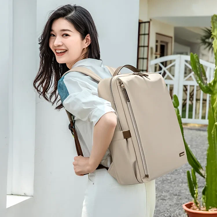 笑顔の女性がベージュの軽量ビジネスリュックを背負い、屋外で快適に立っている様子。多収納で15.6インチ対応。