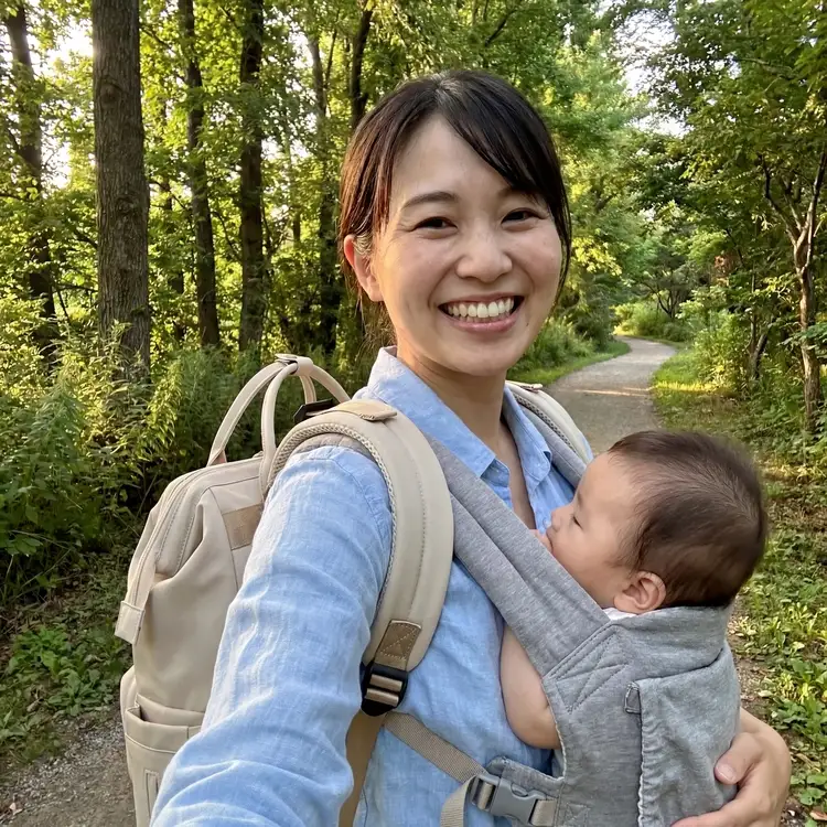 緑豊かな登山道で、赤ちゃんを抱っこ紐で抱え、リュックを背負って笑顔で歩く母親