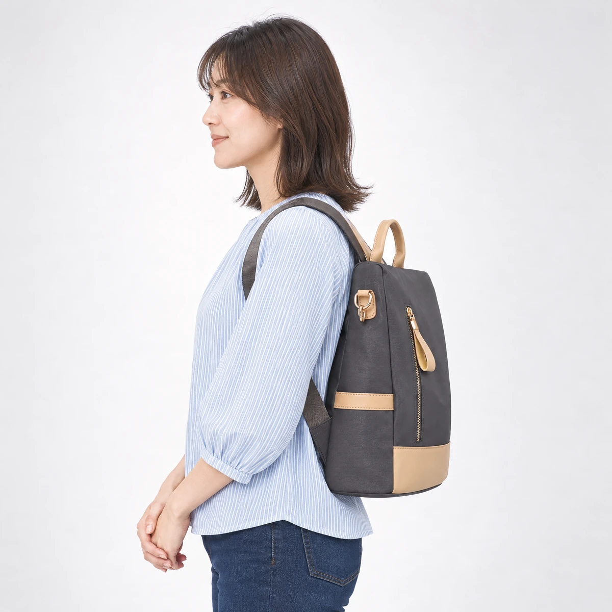 グレーのリュックを背負った横姿。マチ13cmの厚みとサイドのレザーバンド