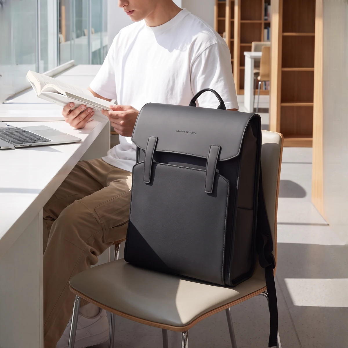 図書館の椅子に置いたビジネスリュックと本を読む男性