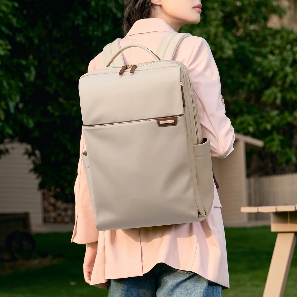 16インチPC対応 A4収納 20L レディース ビジネスリュック 夕暮れの柔らかな光が差し込む庭で、ピンクのブレザーを着た女性が背負う16インチPC対応の20Lレディースビジネスリュック