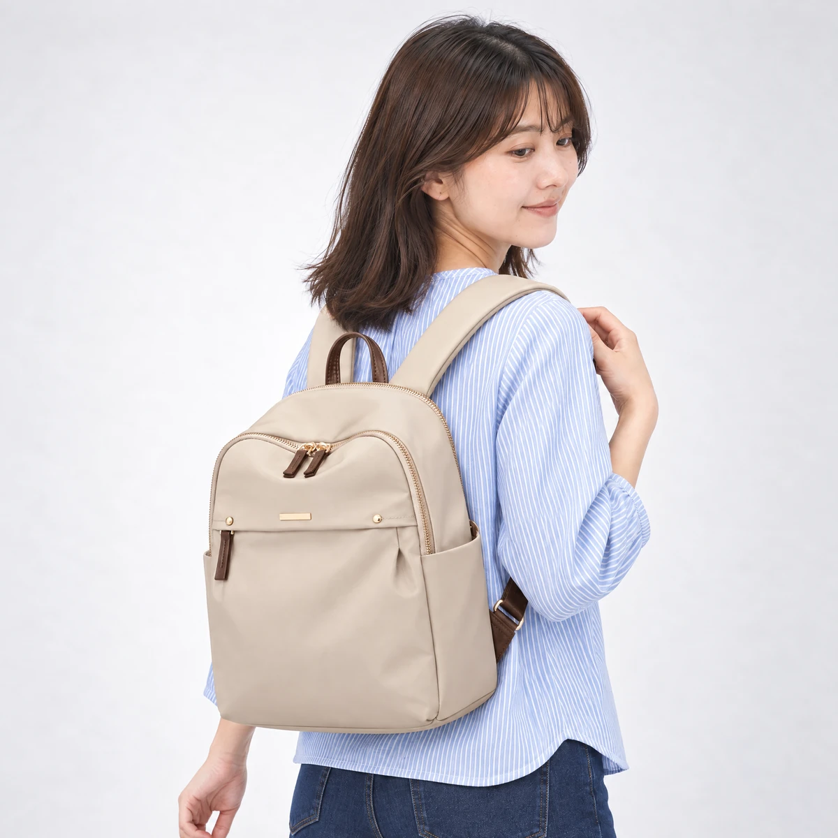 ベージュのリュックを背負った斜め後ろ姿。サイドポケットとマチ12cmの厚み