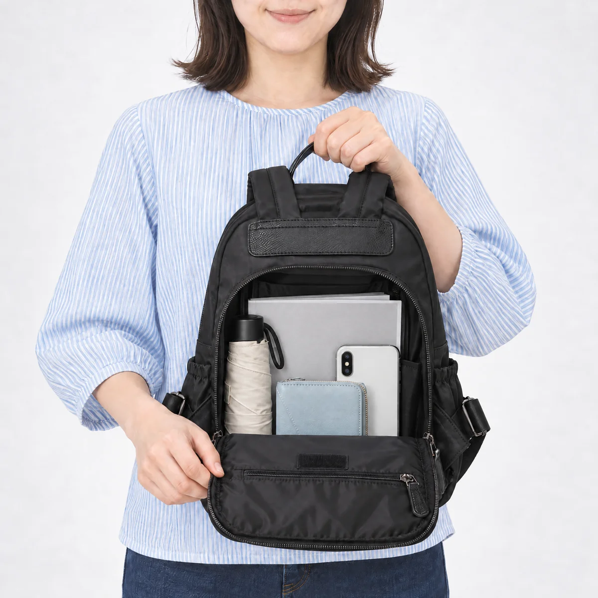背面ファスナーを開けたブラックのミニリュック。A4の雑誌、折りたたみ傘、スマートフォン、財布が入る