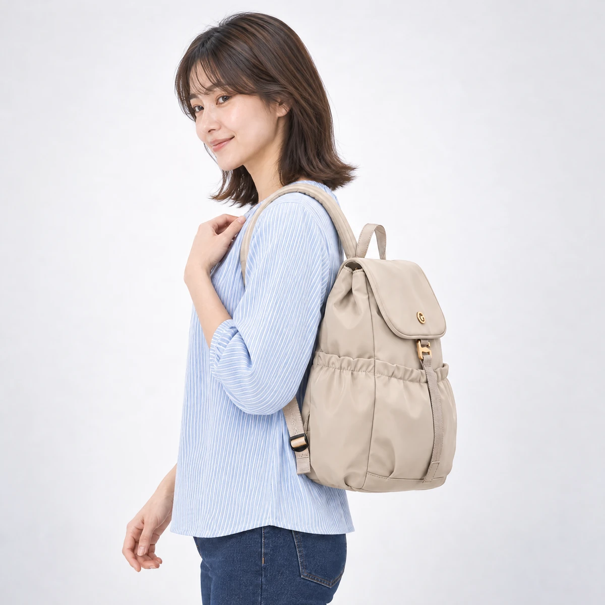 ベージュのリュックを背負った横姿。マチ12cmの厚みとサイドのフリルポケット