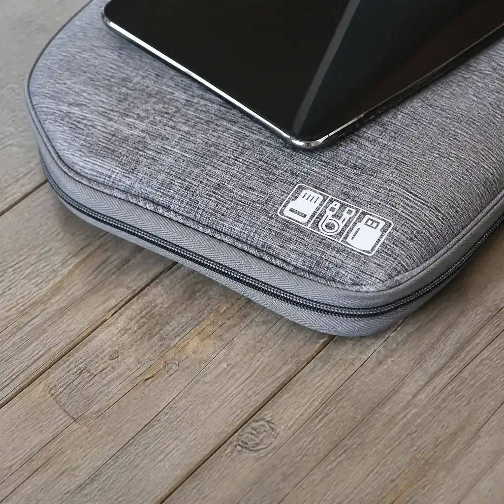 木製の板の上に平置きされたグレーの生活防水ガジェットポーチと、その上に置かれた黒いタブレット。自然光が差し込むミニマルでモダンな整理整頓された仕事空間。