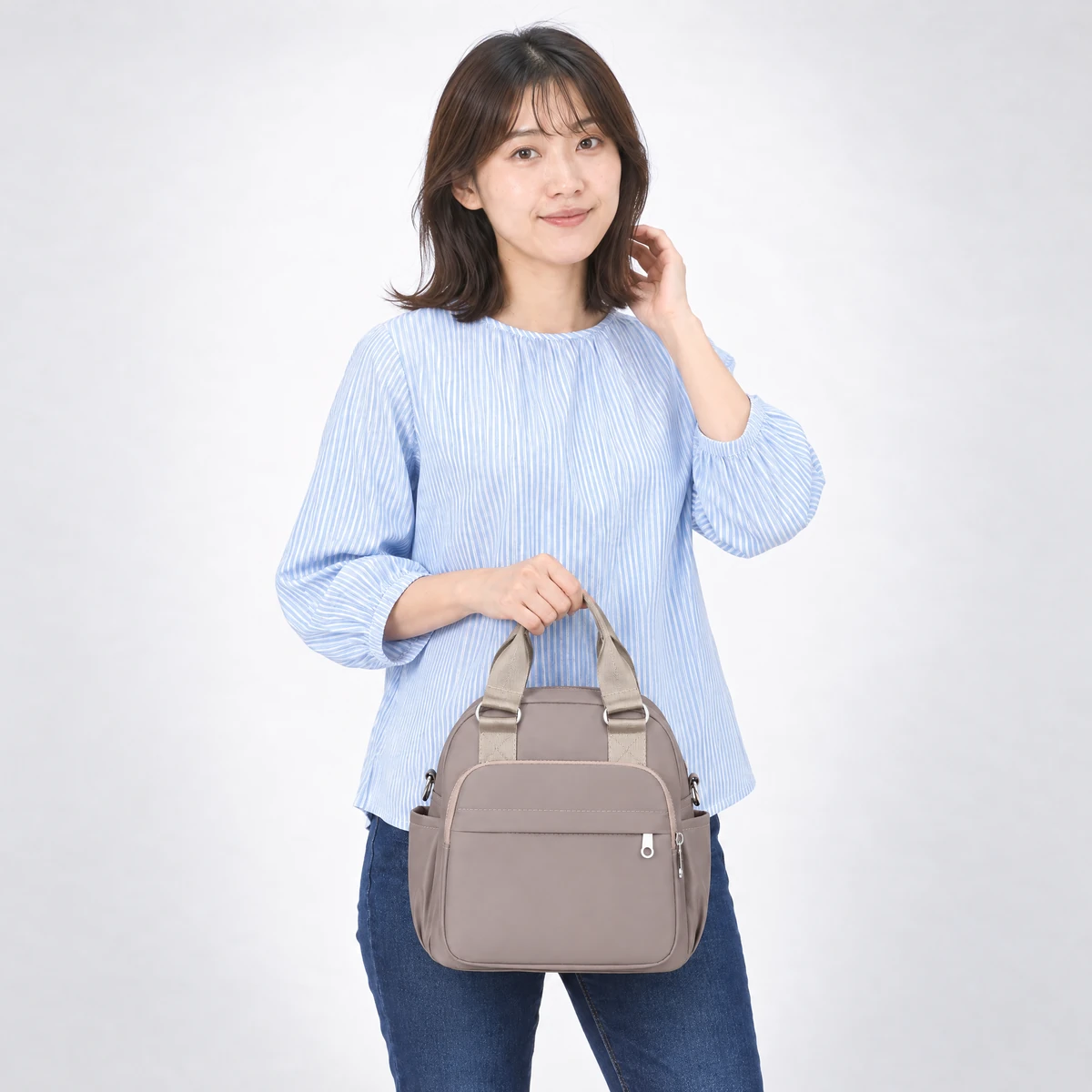 ベージュの3wayバッグを2本の持ち手でハンドバッグとして持つ