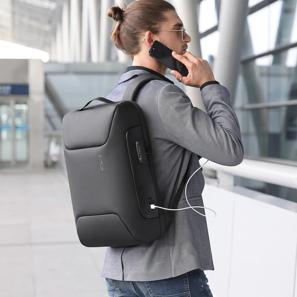 高機能な20L生活防水3WAYメンズビジネスリュック 明るく近代的なターミナルで、グレーのジャケットを着て電話をするビジネスマンが背負う、高機能な20L生活防水3WAYメンズビジネスリュック。