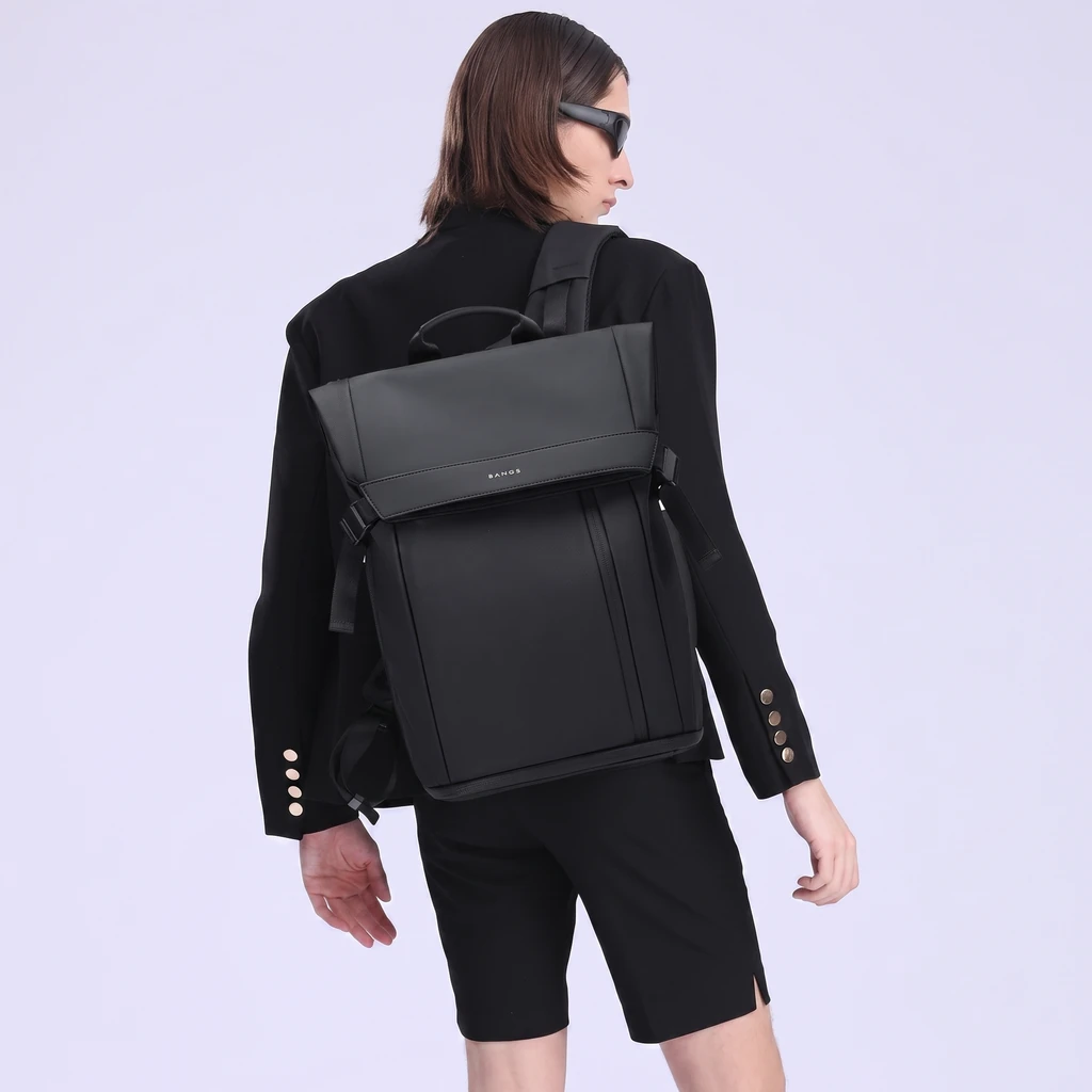 黒いブレザーとサングラス姿のモデルが背負う、洗練されたモダンな20Lメンズビジネスリュック。グレーのスタジオ背景に映える都会的なデザイン。
