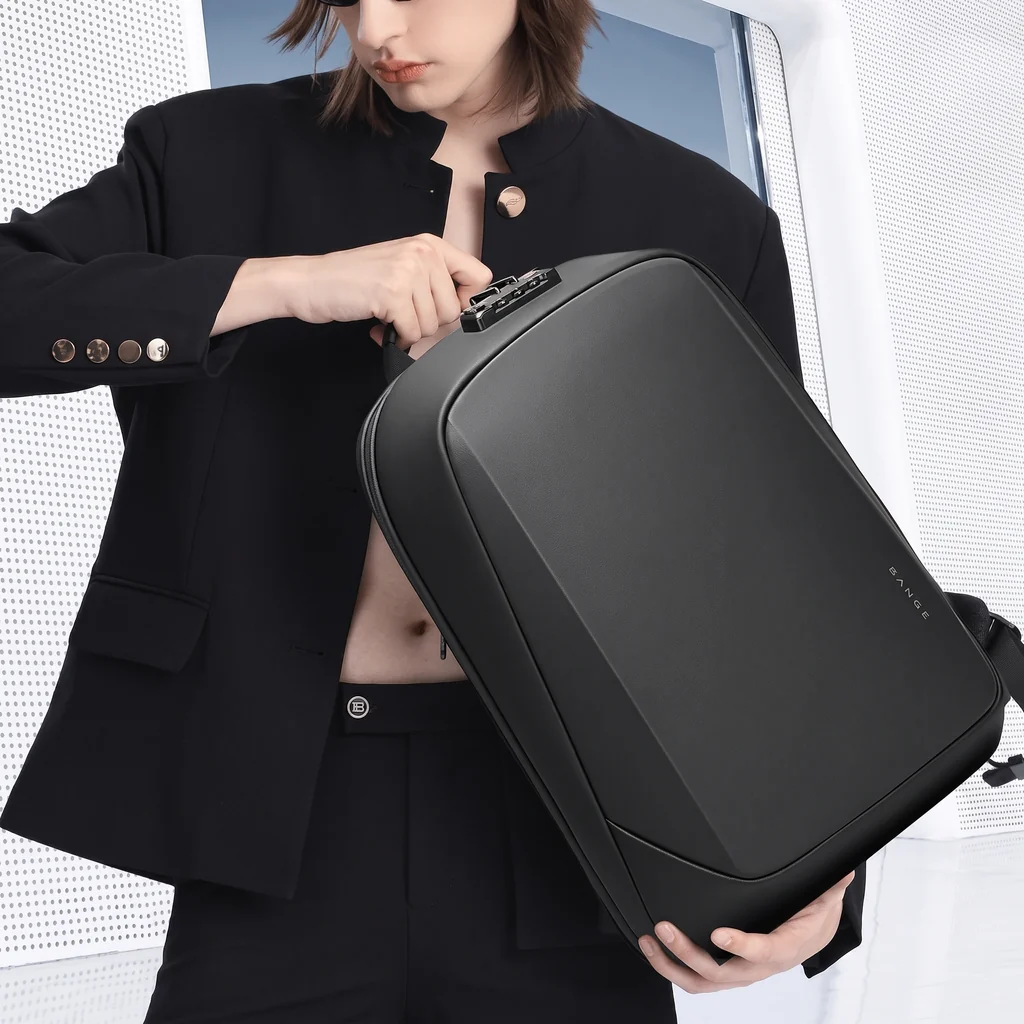 白を基調としたミニマルで近未来的な空間で、黒いブレザーのモデルが持つ15インチ20L防水仕様のメンズPCスマートバックパック。