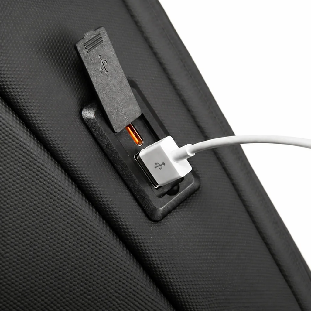 内蔵されたUSB充電ポートに白いケーブルを接続した、スタイリッシュな黒のメンズ用防水PCバックパックのクローズアップ