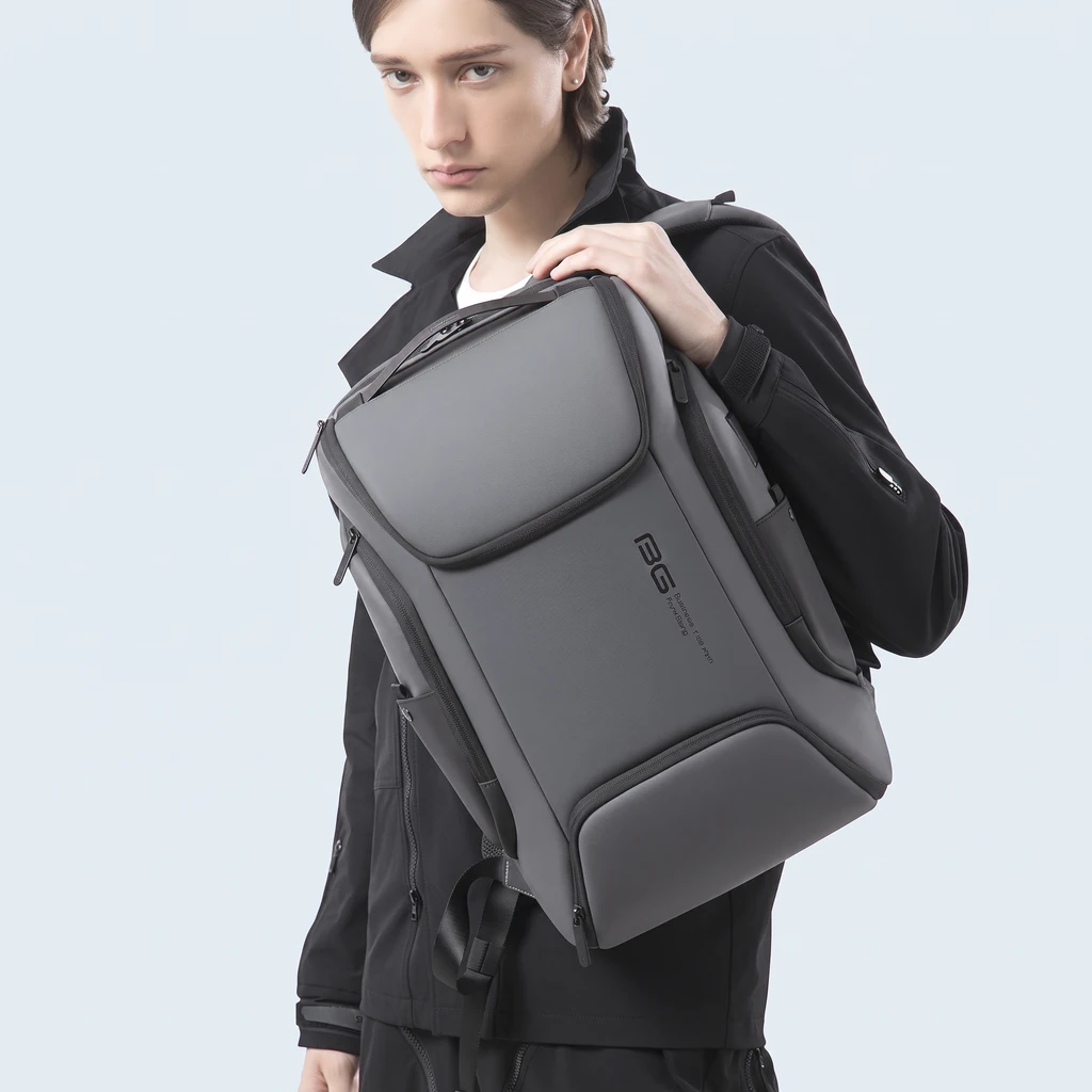 黒いジャケットを着た男性が肩に掛けた、15インチPC対応のミニマルな20L生活防水ビジネスリュック。背景は清潔感のあるライトブルー。