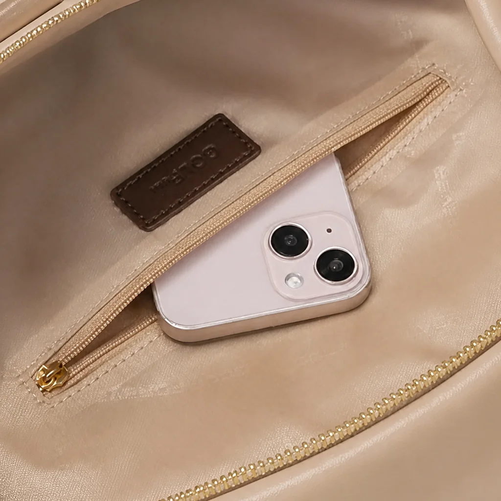 女性用15インチPCリュックのファスナー付き内ポケット。温かみのあるベージュの裏地に映える、ピンクのスマートフォンとゴールドのジッパー。