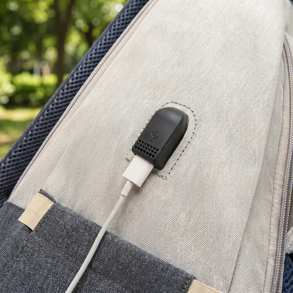 ベージュグレーの多機能マザーズバッグにあるUSBポートに、白い充電ケーブルを接続したメッシュストラップ背景のクローズアップ