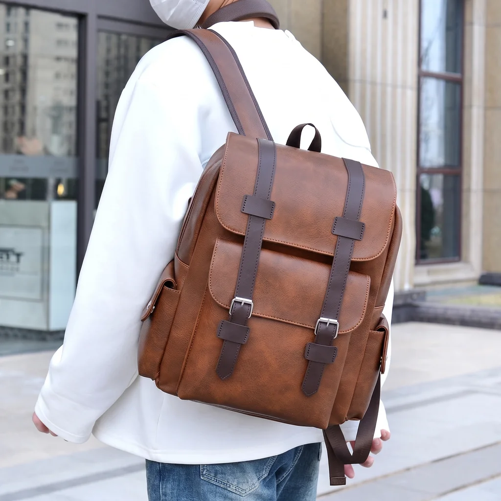 白いスウェットにジーンズ姿の男性が背負う、おしゃれな20L防水仕様のレトロメンズレザーバックパック。洗練されたモダンな都会の街並み。