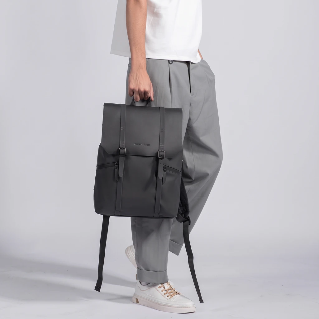 生活防水仕様 メンズ 15インチ対応 20L ビジネスバックパック 白Tシャツにグレーのパンツと白スニーカーを合わせた男性が手にする、生活防水仕様で機能的なメンズ15インチ対応20Lビジネスバックパック。