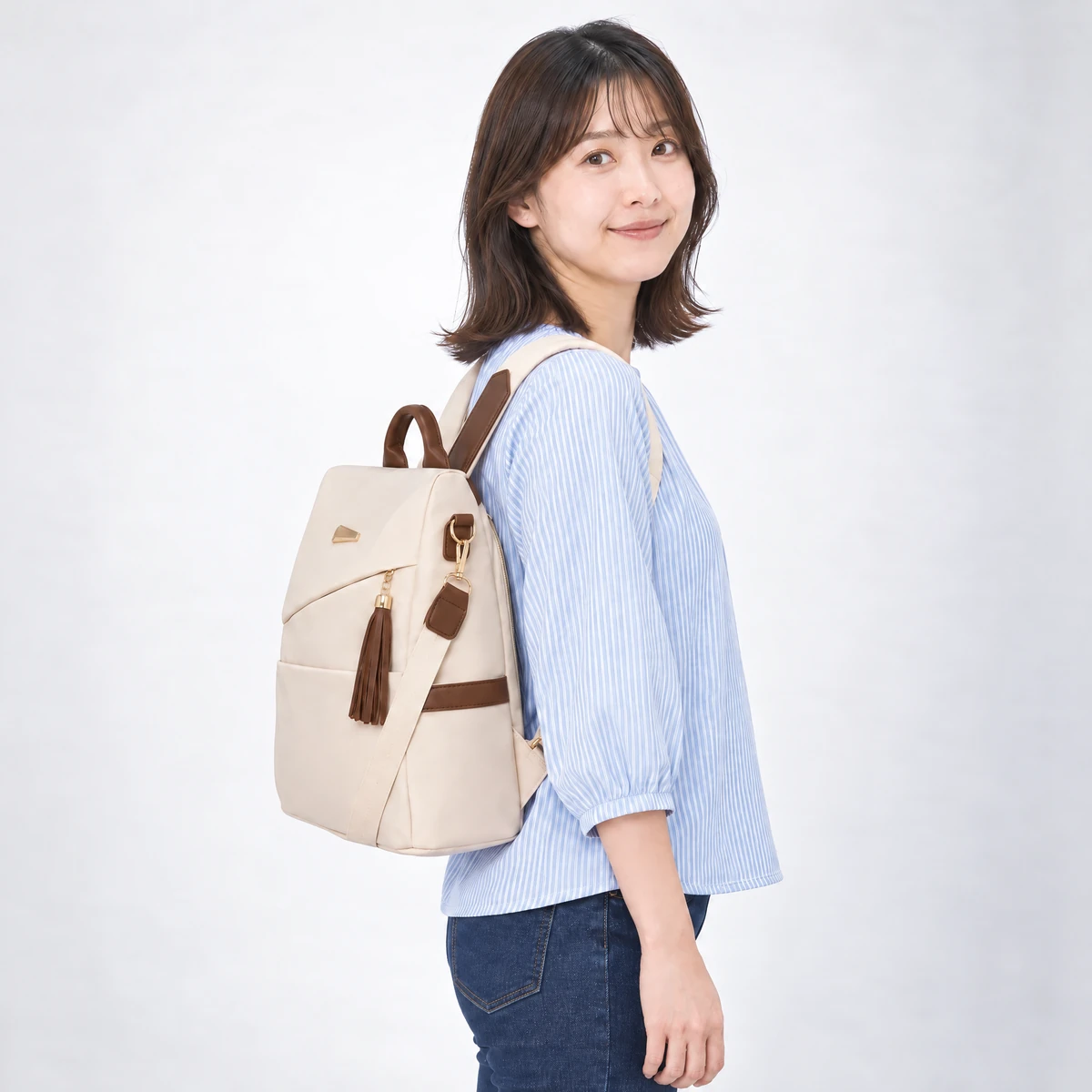 ベージュのリュックを背負った横姿。マチ12cmの厚みとブラウンのサイドバンド