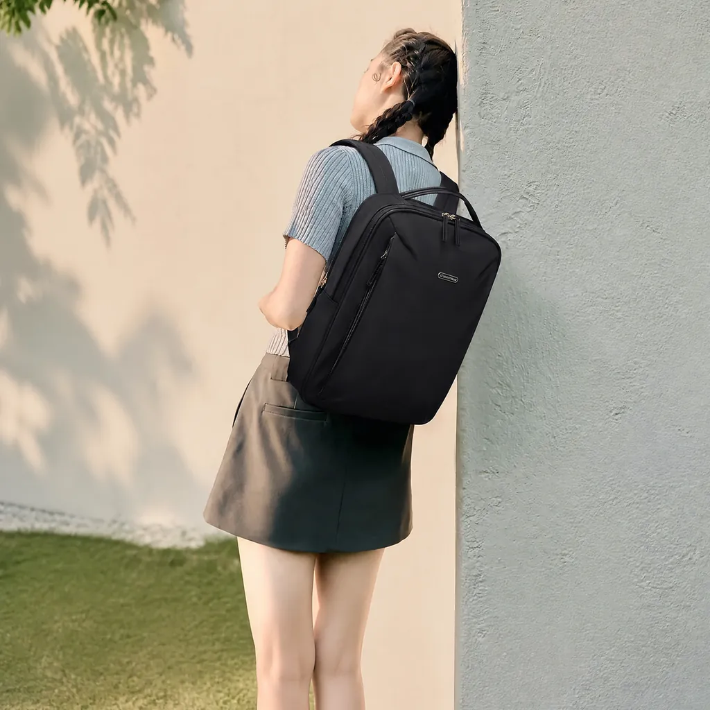 柔らかな午後の日差しが差し込む屋外で、コンクリート柱に寄りかかる女性が使用する15インチ対応の防水薄型PCリュックサック