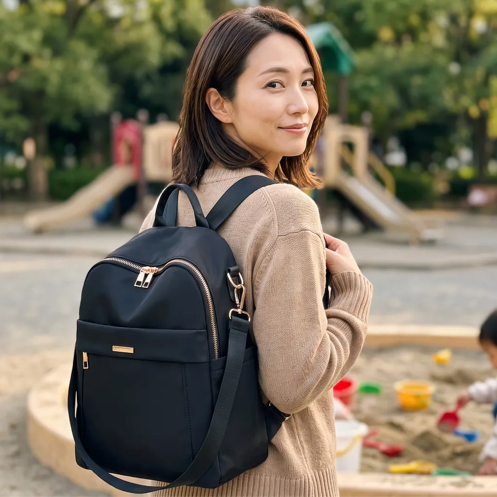 陽の光が届く公園の遊び場で、ベージュの温かみのあるセーターを着て、20Lの生活防水ミニリュックを背負い笑顔で振り返る女性。